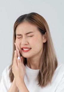 a woman touching her cheek due to tooth pain