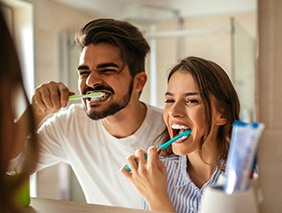 Man and woman brushing teeth at bathroom mirror