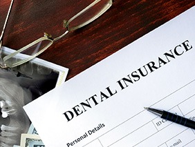 Closeup of top of dental insurance form with pen and glasses