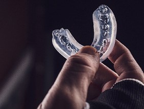Hand holding clear mouthguard with dark background