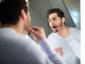 Man with lost dental crown looking at smile in mirror