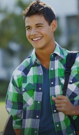 Young smiling man in plaid shirt holding backpack outdoors