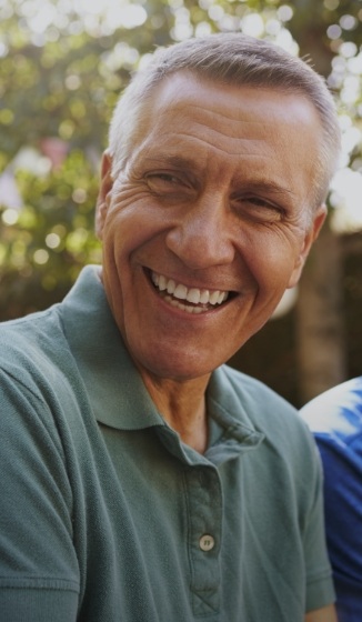 Older man in green polo shirt laughing outdoors