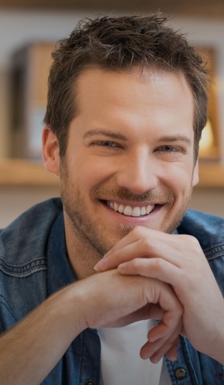 Young smiling man sitting down and resting his chin on his hands