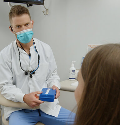 Dentist holding a small blue box while talking to dental patient in Broken Arrow