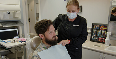 Dental team member putting protective sheet over patient's clothes