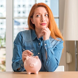 Woman putting coin in piggy bank for cost of Invisalign in Broken Arrow