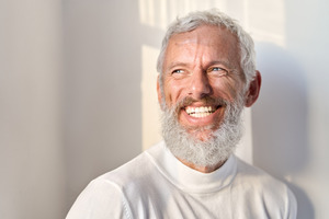 Close-up of a bearded man with a white sweater smiling