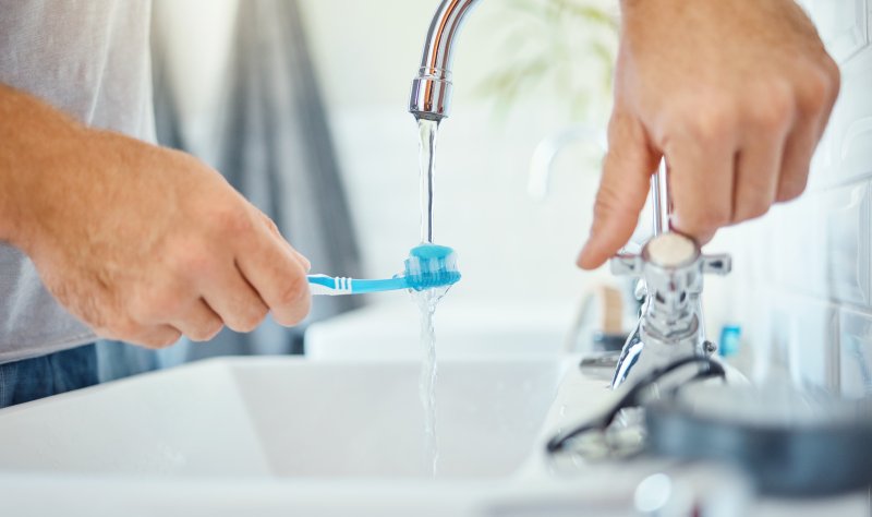 Hands, a toothbrush, and a person at tap for water